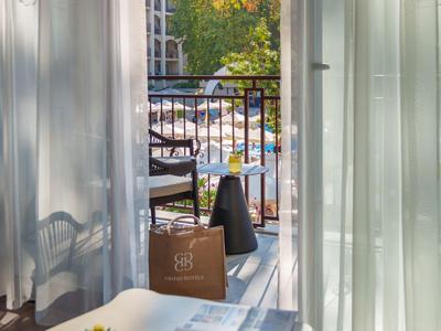 Blick von einem Hotelzimmer auf einen Balkon mit einem Tisch, Sessel und einer grünen Pflanze.