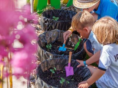 Zwei Kinder pflanzen Pflanzen in Töpfe, begleitet von einem Erwachsenen im Freien.
