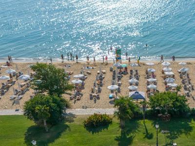Strand mit Sonnenschirmen, Liegestühlen und Menschen am glitzernden Meer an einem sonnigen Tag.