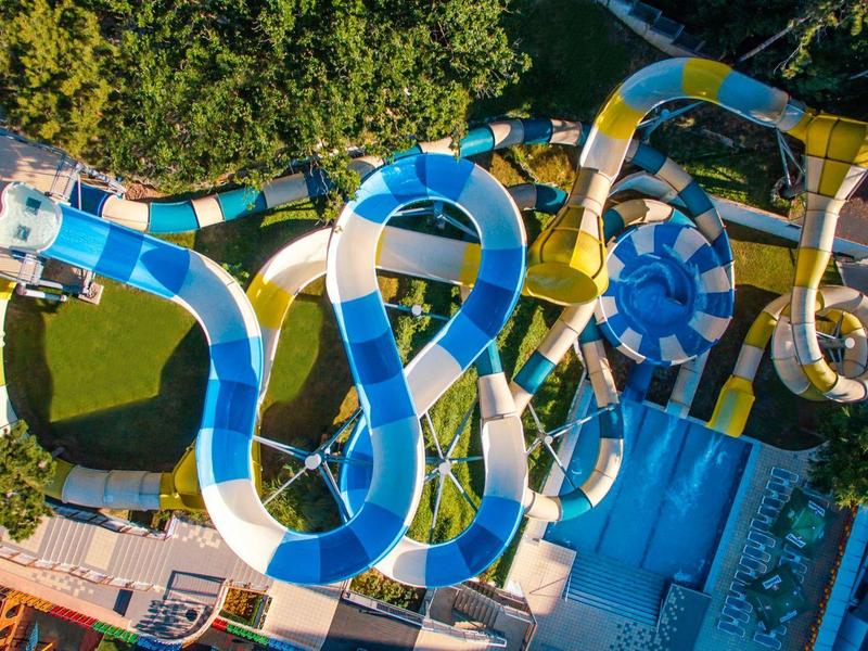 Luchtfoto van een glijbaan in een waterpark met blauwe en witte strepen, omringd door groene bomen.