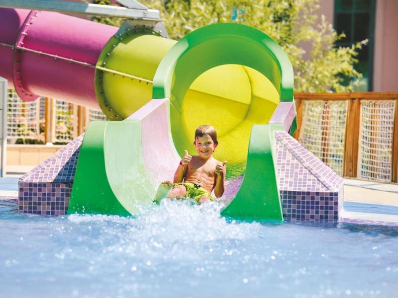 Kind lacht terwijl hij van een kleurrijke glijbaan in een zwembad glijdt