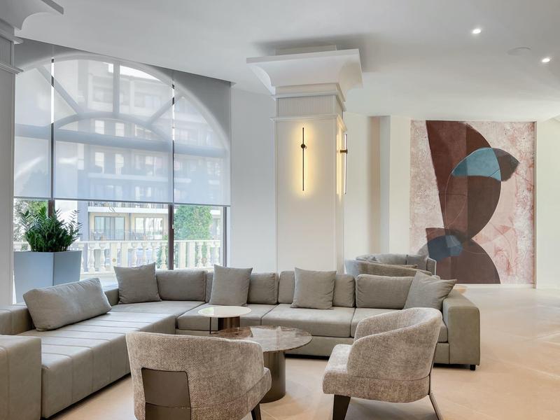 Moderne woonkamer met grote grijze hoekbank, twee fauteuils en groot raam met uitzicht naar buiten.