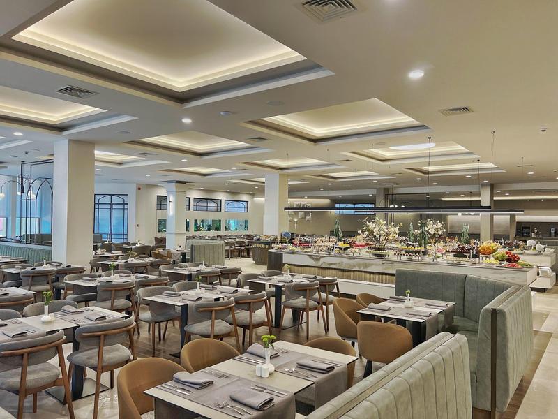 Lichte, moderne hotel eetruimte met vele tafels, stoelen en een buffetstation.