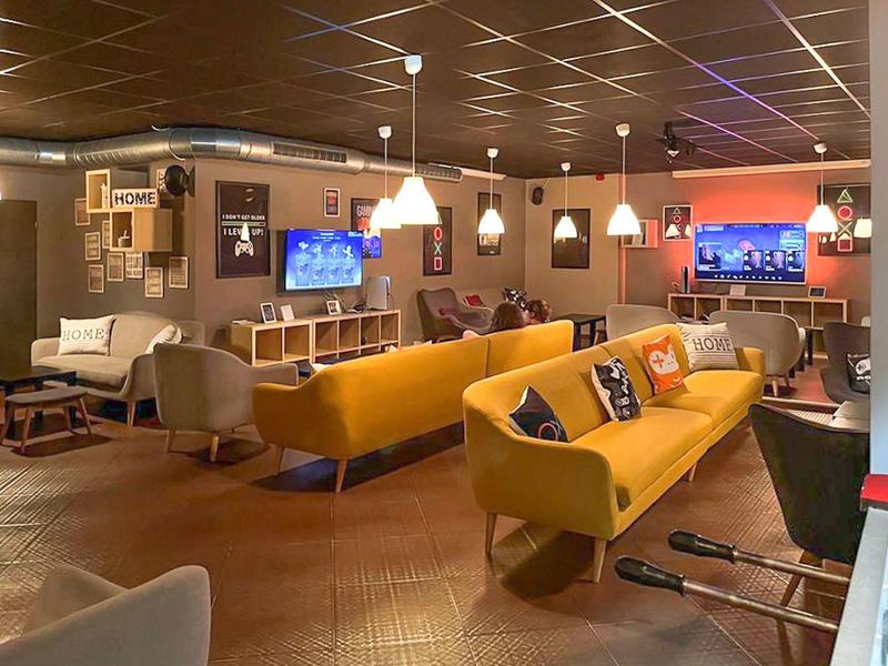 Moderne hotellounge met gele banken, hanglampen en tv-schermen in een gezellige sfeer.