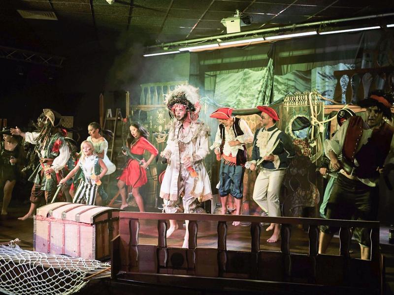 Theaterscène met acteurs in piratenkostuums op het podium met een kist en netten.