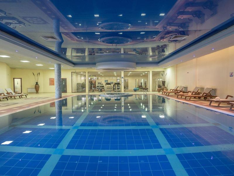 Groot overdekt zwembad met blauwe tegels, ligstoelen en gezellige verlichting