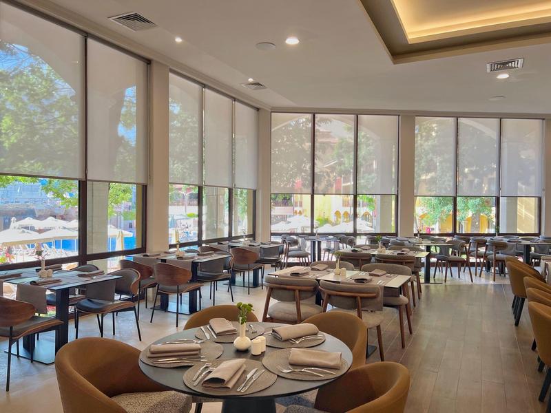 Lichte, moderne eetzaal met grote ramen en gedekte tafels.