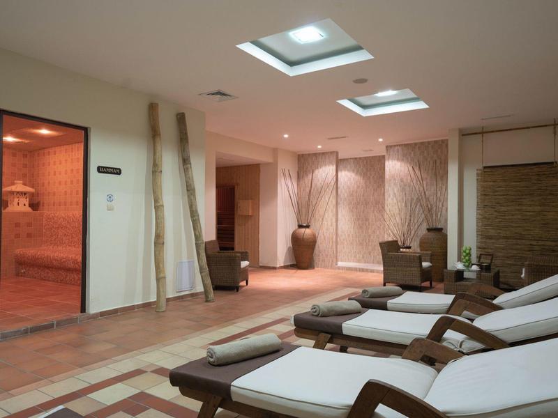 Lichte wellnessruimte met ligstoelen en toegang tot een sauna met rood licht.