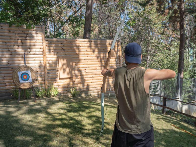Persoon staat in de tuin en richt met boog en pijl op een doelwit.