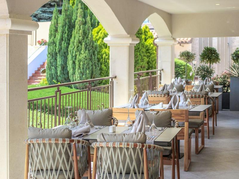 Overdekt terras met eetgedeelte en uitzicht op een groene tuin met bomen.