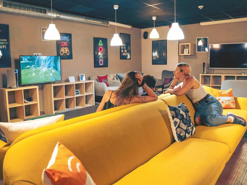 Twee vrouwen ontspannen op een gele bank in een gezellige, moderne woonkamer.