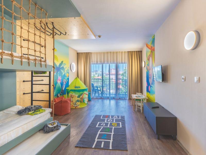 Licht ingerichte kinderkamer met stapelbed, speelkleed en toegang tot balkon.