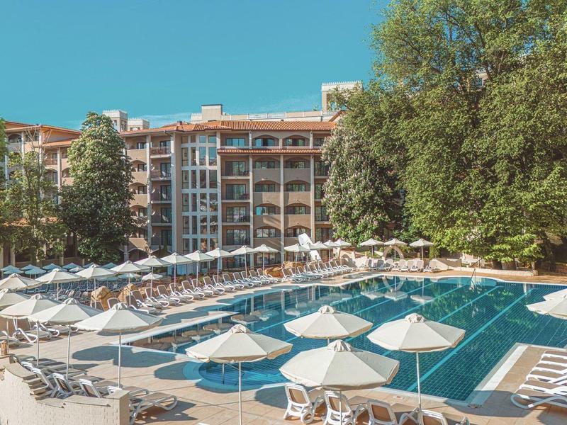 Buitenzwembad met ligstoelen en parasols voor een meerlaagse hotelgebouw en bomen