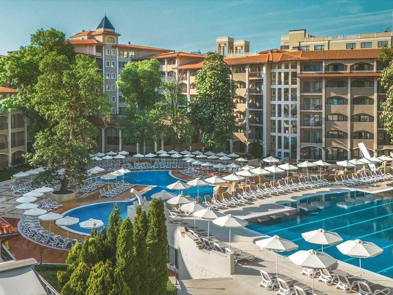 Hotel met buitenzwembad, ligstoelen en parasols voor een meerlaagse gebouw in daglicht.