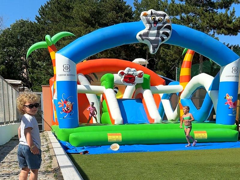 Kind staat naast opgeblazen speeltuin buiten op een zonnige dag.