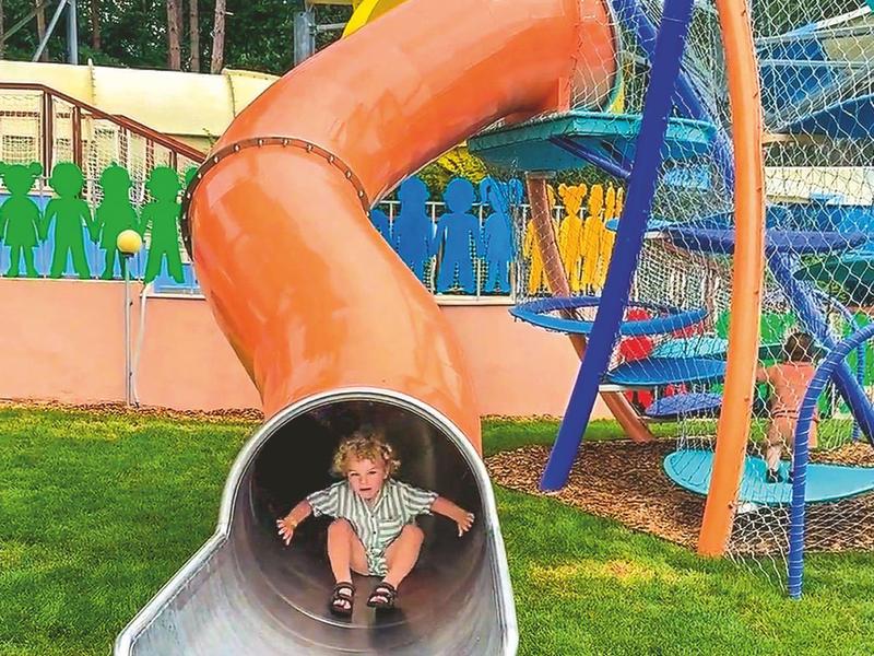 Kind vrolijk glijdend van een kleurrijke, spiraalvormige glijbaan buiten.