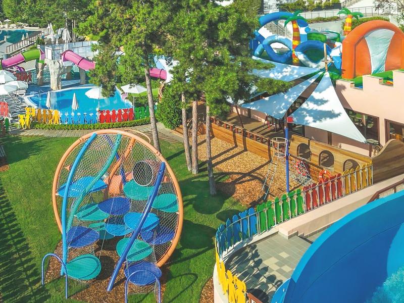 Kleurrijk buitengebied van een waterpark met glijbanen, speeltoestellen en bomen.