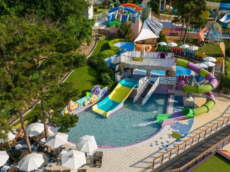 Kleurrijke waterspeeltuin met glijbanen en zwembad in een buitenruimte met parasols.