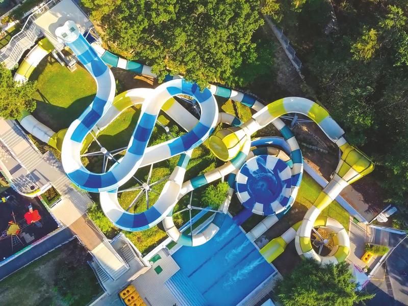 Luchtfoto van een waterpark met kronkelige glijbanen en zwembaden omgeven door bomen.