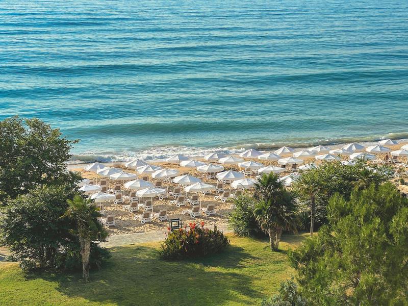 Strand met witte parasols, zand en helderblauw water, omgeven door groen.