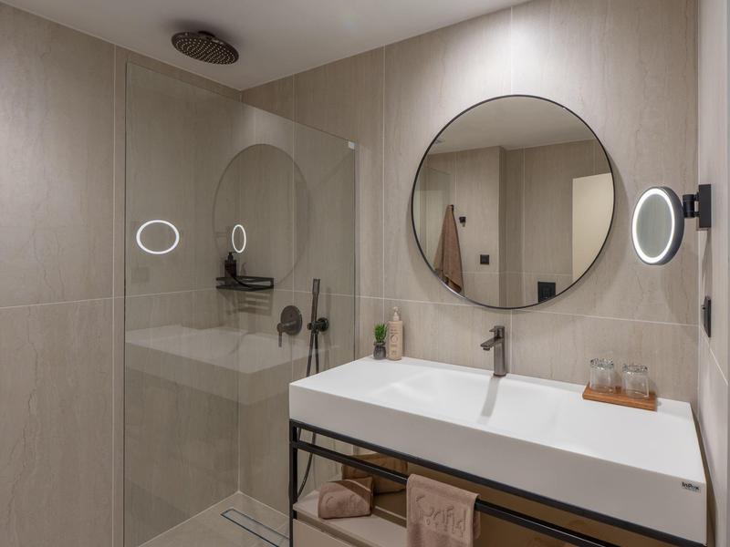 Moderne badkamer met ronde spiegel, glazen douche en grote wastafel op een donker metalen frame.