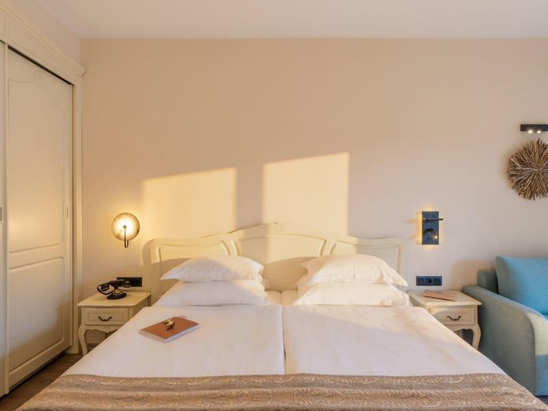 Gezellige hotelkamer met twee bedden, nachtkastjes en een blauwe fauteuil.