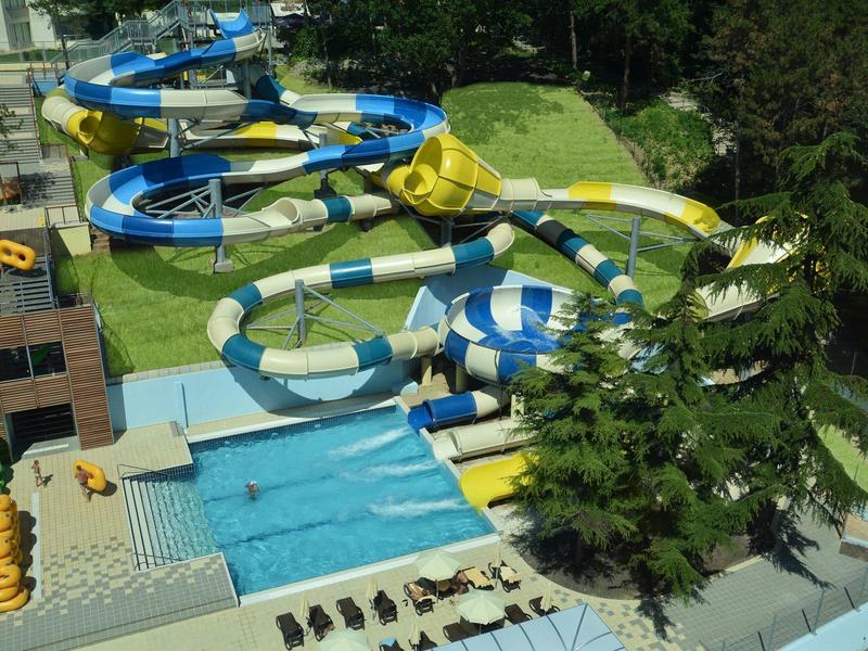 Glijbanen en zwembadgebied in een outdoor waterpark naast een bosgebied.