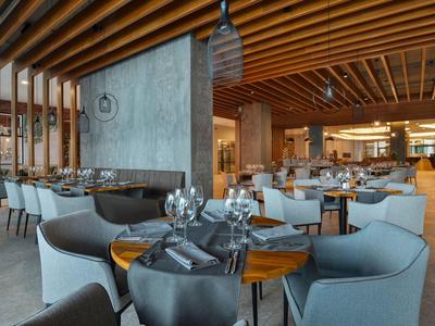 Modernes Restaurant mit Holzbalkendecke, grauen Stühlen und runden Holztischen, elegant gedeckt.