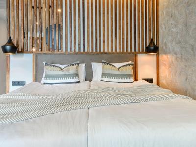 Modernes Schlafzimmer mit großem Bett, weißen Kissen, Holzwand und Betonwand im Hintergrund.