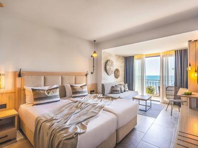 Modernes Hotelzimmer mit zwei Betten, großem Fenster und Meerblick, hellen Holzmöbeln und sanfter Beleuchtung.