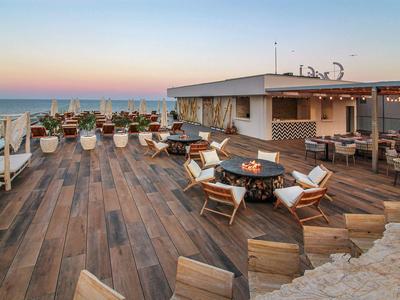 Große Hotelterrasse mit Holzboden, Sitzgruppen und Blick auf das Meer bei Sonnenuntergang.