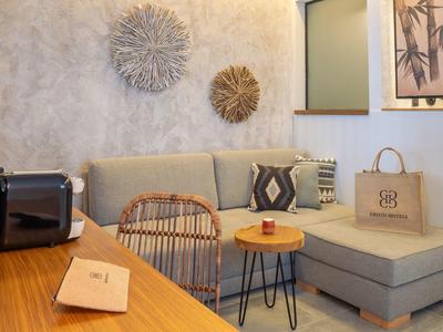 Gemütliche Sitzecke mit grauem Sofa, Holz- und Metalltisch, Bambusstuhl und dekorativer Wandgestaltung.