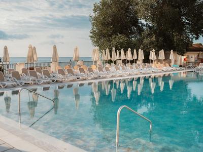 Prázdný bazén s mnoha lehátky a zavřenými slunečníky na pláži pod zataženou oblohou.