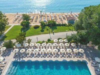 View of a pool with white umbrellas and beyond it a sandy beach by the sea.