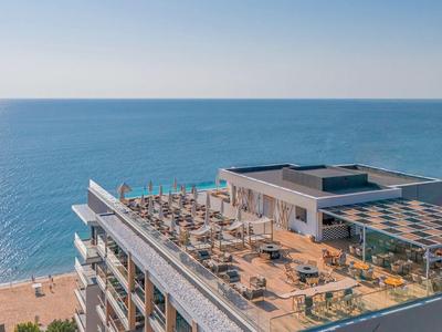 Hotel rooftop terrace with sun loungers overlooking the sea under a clear sky.