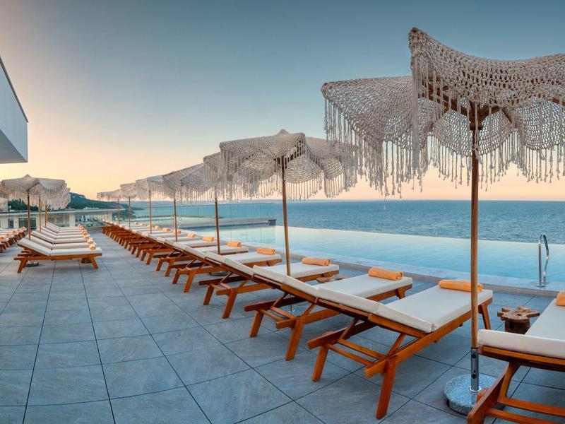 Moderní terasa s lehátky a slunečníky u moře při západu slunce.