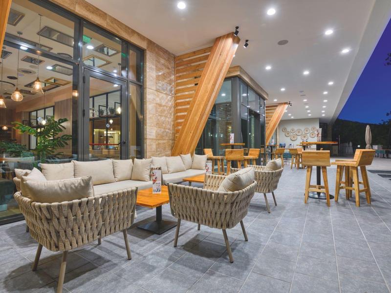 Pohodlná venkovní terasa hotelu s moderním posezením a dřevěnými stolky při soumraku.