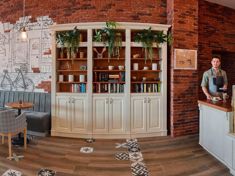 Moderní kavárna s dřevěnými stěnami, bílým pultem a posezením se židlemi a stoly.