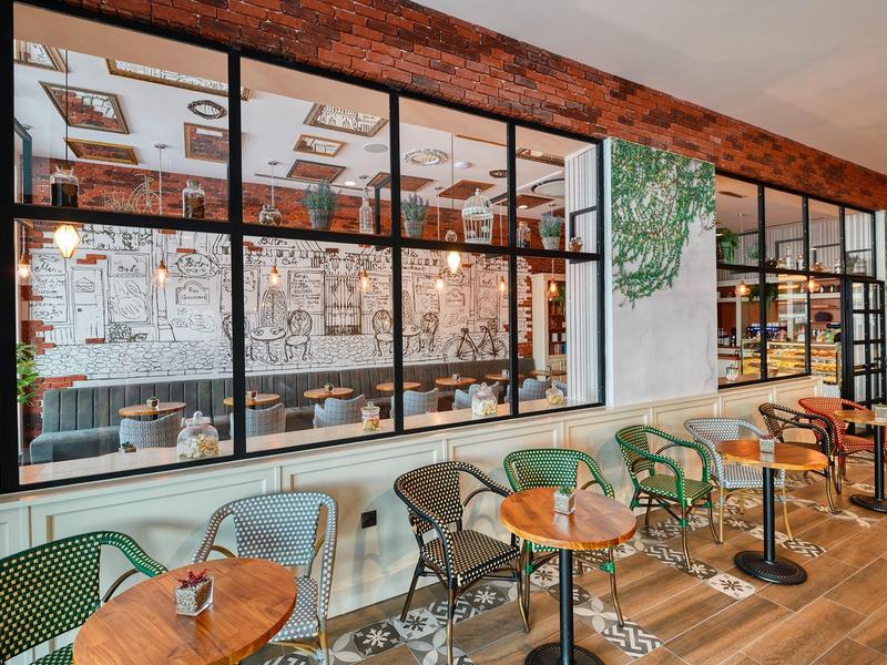 Moderní restaurace s dřevěnými podlahami, zelenými židlemi a velkými okny.