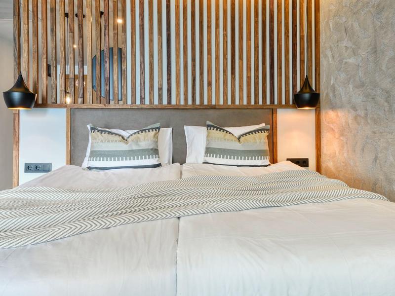 Moderní hotelový pokoj se dvěma postelemi a dekorativním dřevěným panelem za čelem postele.