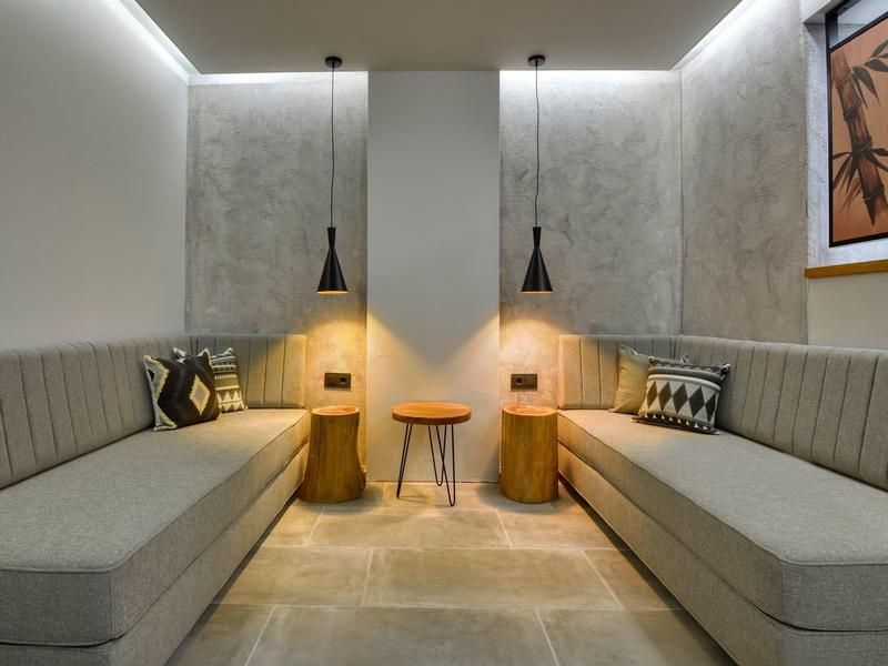 Jednoduchý salón s šedými pohovkami, dřevěnými stolky a teplým osvětlením v útulné místnosti.