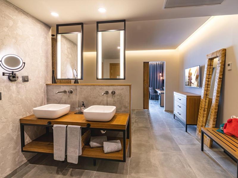 Moderní koupelna s dvojitým umyvadlem, velkými zrcadly a dřevěnou policí.