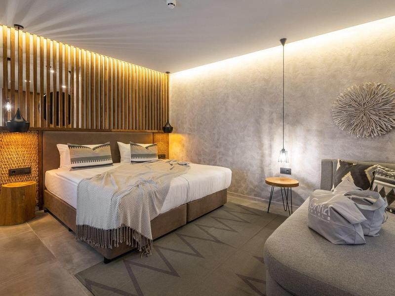 Moderní hotelový pokoj s manželskou postelí, pohodlným posezením a atmosférickým osvětlením.