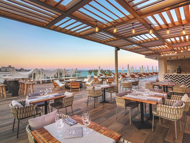 Střešní terasa s prostřenými stoly a výhledem na město za západu slunce.