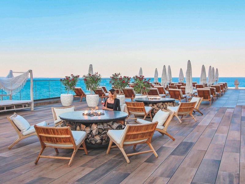 Terasa s dřevěnými židlemi a stoly u moře pod modrou oblohou v hotelovém resortu.
