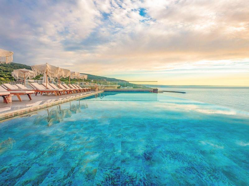 Nekonečný bazén s lehátky u moře při západu slunce