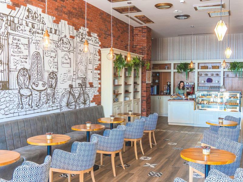 Moderní kavárna s modrými křesly, dřevěnými stoly a černobílou nástěnnou malbou.