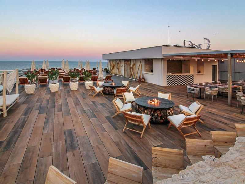 Moderní střešní terasa s dřevěnou podlahou, posezením a výhledem na moře při západu slunce.