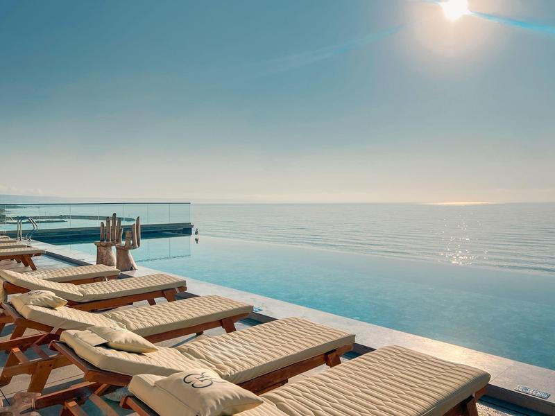 Lehátka u nekonečného bazénu s výhledem na moře za jasné oblohy.