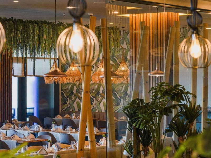 Moderní restaurace s teplým osvětlením a množstvím rostlin uvnitř.